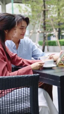 Genç çift açık bir kafede tablet ve kahveyi paylaşırken neşeli bir anın tadını çıkarıyor.