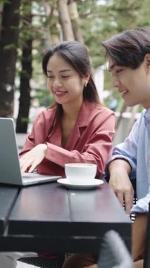 Genç Asyalı çift Bangkok, Tayland 'da bir masada dizüstü bilgisayar üzerinde çalışıyor ve kahve içiyorlar.