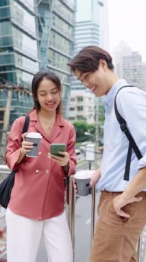 Genç çift şehirde bir köprüde duruyor, kahve içiyor ve akıllı telefona bakıyor.