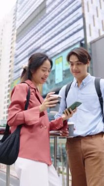 Genç bir çift şehir caddesinde durmuş, kahve içiyor ve akıllı telefondan bir şeye bakıyor.