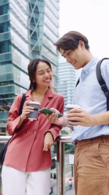Genç çift şehirde bir köprüde duruyor, kahve içiyor ve akıllı telefona bakıyor.