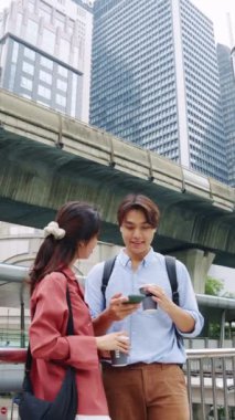 Genç Asyalı çift şehir merkezinde durmuş kahvelerini yudumluyor ve ağır çekimde akıllı telefon kullanıyorlar.