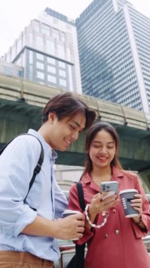 Genç çift Bangkok 'ta bir anın tadını çıkarıyor, akıllı telefona bakıyor ve ağır çekimde gülümsüyor.