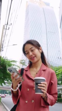 İş kadını elinde kahve fincanıyla ağır çekimde yürüyor ve mesaj atıyor.