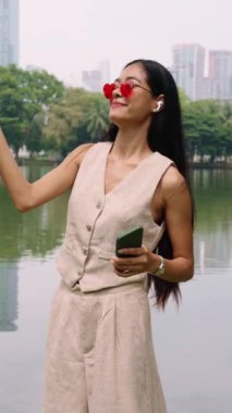 Kalp şeklinde güneş gözlüğü takan genç bir kadın parkta müzik dinlemekten hoşlanıyor.