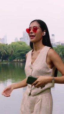 Kalp şeklinde güneş gözlüğü ve kulaklık takan genç bir kadın ağır çekimde neşeyle dans ediyor.