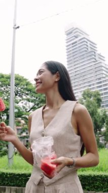 Neşeli kadın, şehir mimarisi ve yeşilliklerle çevrili, bereketli bir şehir parkında karpuz yemekten hoşlanıyor.