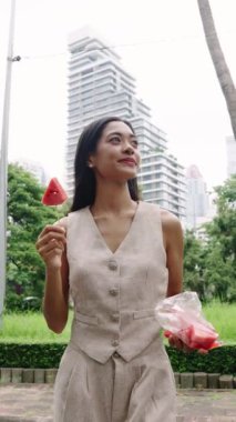 Genç bir kadın şehir caddesinde ferahlatıcı bir karpuz atıştırmasının tadını çıkarıyor.