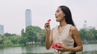 Bangkok 'ta bir gölün kenarındaki çubukta karpuzun tadını çıkaran genç bir kadın, doğal ışık altında ağır çekimde yakalandı.