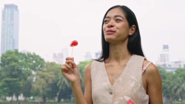 Bangkok parkındaki bir çubukta şekerli meyvenin tadını çıkaran genç bir kadın, açık havada canlı bir ortamda ağır çekimde yakalandı.