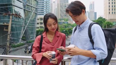 Akıllı telefon kullanan ve Bangkok 'ta bir köprüde kahve içen genç bir adam ve kadının yavaş çekim sahnesi.