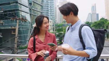 Genç çift şehirde bir köprüde duruyor, kahve içiyorlar ve ağır çekimde akıllı telefona bakıyorlar.