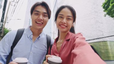 Elinde kahve fincanları olan genç bir adam ve kadın ağır çekimde selfie çekerken gülümsüyorlar.