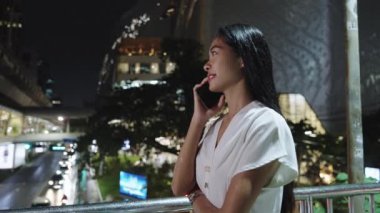 İş kadını, Bangkok 'ta canlı bir akşamda şehir ışıklarıyla çevrili keyifli bir telefon görüşmesi yapmaktan hoşlanıyor.
