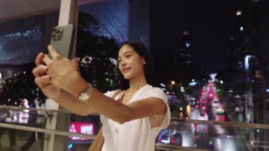 İş kadını, şehir ışıkları ve şehir enerjisiyle çevrili canlı bir bangkok 'ta akıllı telefonuyla selfie çekiyor.