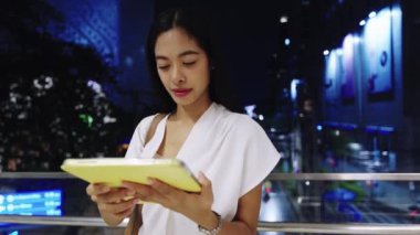 Genç Asyalı iş kadını geceleri Bangkok, Tayland 'da tablet kullanıyor, modern bir şehir yaşam tarzı sergiliyor.