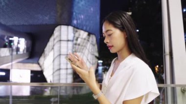 Bangkok, Tayland 'da gece akıllı telefon kullanan genç bir iş kadını modern şehir yaşam tarzını gözler önüne seriyor.