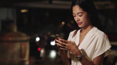 Genç iş kadını Bangkok 'ta gece akıllı telefonunu kullanarak canlı şehir atmosferinin tadını çıkarıyordu.