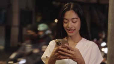 Genç iş kadını, Bangkok, Tayland 'ın şehir eyleminin ortasında gece telefonuyla mutlu mesut mesajlaşıyor.