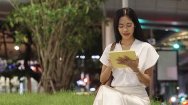 İş kadını geceleri Bangkok 'ta bir çimenlikte oturuyor, tablete bakıyor ve gülümsüyor.