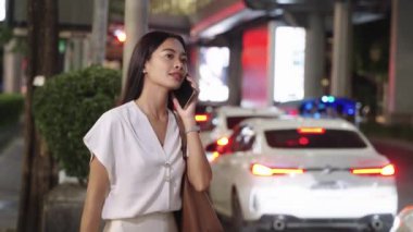 Genç Asyalı iş kadını, Bangkok 'ta kalabalık bir caddede yürürken telefonuyla hoş bir sohbet ediyor.