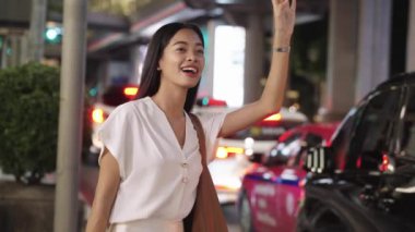 Genç iş kadını, Bangkok caddesinde taksiyi selamlıyor. Şehir hayatı ve profesyonel güvenini gösteriyor.