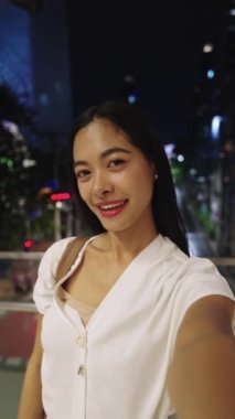 Gece bangkok 'ta gökyüzünde selfie çeken genç bir iş kadını. Etrafı canlı şehir ışıkları ve şehir enerjisiyle çevrili.