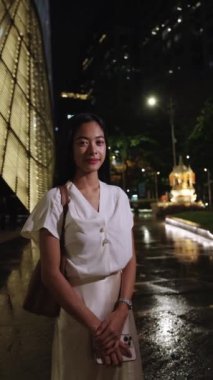 Gülümseyen iş kadını gece Bangkok 'un canlı sokaklarında duruyor, şehirlerin canlı atmosferini gösteriyor.