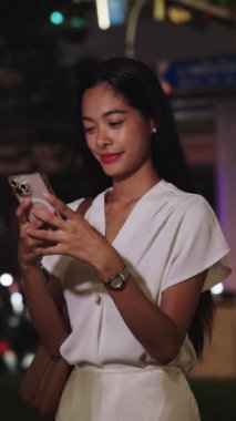 Şehir gecesindeki iş kadını, modern şehir yaşamını yansıtan canlı Bangkok 'ta akıllı telefonuna mutlu mesajlar atıyor.