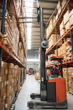 Lojistik operatörü büyük bir depoda raflardaki malları düzenleyen bir forklift kullanıyor.