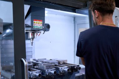 Metal işçisi, metalurji kumaşında özel mekanik parçalar üreten bir cnc değirmen makinesini kontrol ediyor.