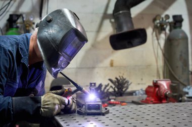 Yetenekli kaynakçı titizlikle bir tezgahta metal bileşenleri birleştiriyor kaynak makinesini kullanıyor ve atölye ortamında koruyucu giysiler giyiyor.