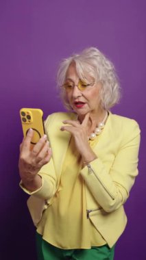 Modaya uygun bir son sınıf öğrencisi yeşil ekran akıllı telefonuyla canlı mor bir arka plana karşı poz veriyor.