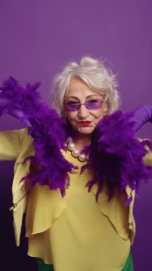 Canlı mor bir arka plana karşı oyuncu pozlar veren son sınıf öğrencisi bir kadın, kendine güvenini ve tarzını sergiliyor.