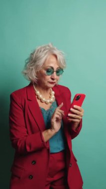 İş kadını çeşitli pozlar verirken canlı bir turkuaz arka plana karşı akıllı telefon kullanıyor.