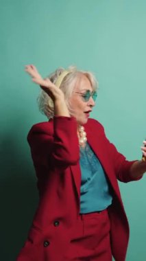 Ruhlu yaşlı kadın kulaklıkla müzik dinlerken mutluluk ve canlılığını ifade ederek neşeyle dans ediyor. Yaşı kucaklama, müzik keyfi ve neşeli ruh kavramları için mükemmel.
