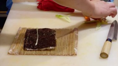 Şef usta bir şekilde suşi rulolarını bambu hasırında taze sebzelerle birleştiriyor. Profesyonel bir mutfakta geleneksel teknikleri kullanarak.