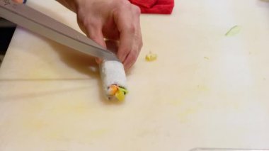 Şef ustaca bir suşi rulosunu dilimleyerek beyaz bir kesim tahtasının üzerinde küçük parçalara ayırıyor, mutfak uzmanlığı gösteriyor.