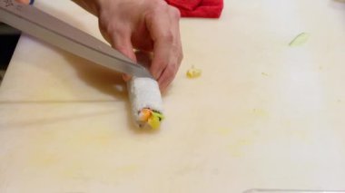 Şef ustaca bir suşi rulosunu dilimleyip, beyaz bir kesim tahtasının üzerinde küçük parçalara ayırıyor, aşçılık uzmanlığı gösteriyor.