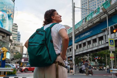 Sırt çantalı kadın turist Bangkok 'un canlı sokaklarını keşfediyor, bir batakhanenin yakınındaki şehir manzarasına bakıyor, kentsel atmosferi kucaklıyor.