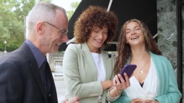 Bir grup iş adamı binanın dışında dikiliyor, akıllı telefon kullanıyor ve selfie çekiyorlar.