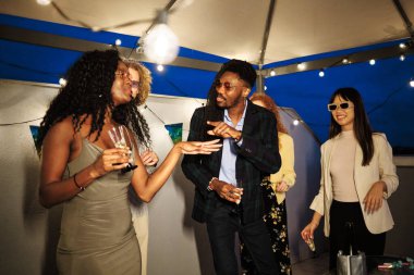 Neşeli çoklu etnik arkadaşlar çatı katındaki bir partide dans edip şampanya içiyorlar.