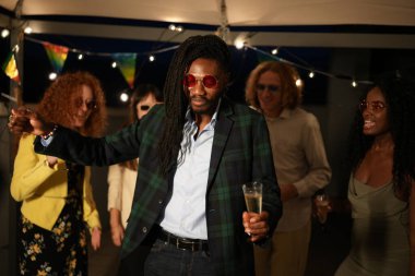 Bir grup etnik çeşitlilikte arkadaş çatı katındaki bir partide dans edip şampanya içiyorlar.