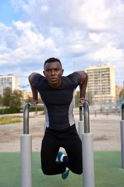 Bir jimnastik parkındaki paralel barlara dalarak vücudunun üst kısmını güçlendirmeye odaklanmış sporcu, sağlıklı yaşam tarzı ve uygunluğu teşvik ediyor.