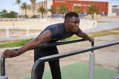 Açık hava spor salonunda spor yaparken kollarını paralel barlara uzatan konsantre sporcu.