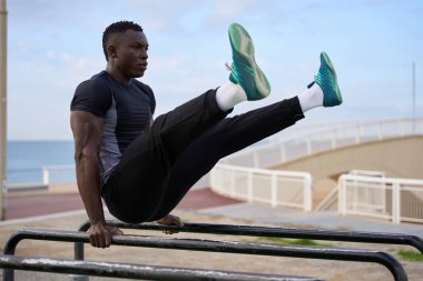 Açık havada sporcu eğitimine odaklanmış, güç ve denge gösterisi sergiliyor. Sahildeki arka planda paralel barlar üzerinde etkileyici bir egzersiz yapıyorum.