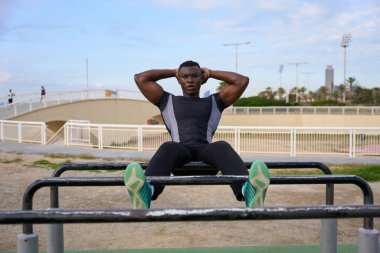 Açık hava spor alanındaki paralel barlarda spor yaparak karın kaslarını güçlendiren odaklanmış siyah sporcu.