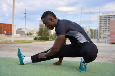 Kentsel çevrede yoğun jimnastik egzersizinden sonra bacaklarını esneten odaklanmış siyah sporcu.