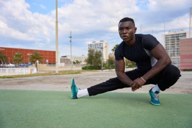 Kentsel çevrede yapılan yoğun jimnastik çalışmalarından sonra bacaklarını esneten kararlı erkek sporcu.