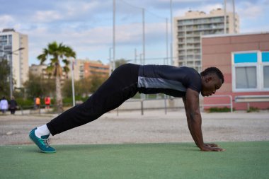 Genç sporcu, şehir parkında yeşil bir minder üzerinde spor tahtası alıştırması yapıyor.